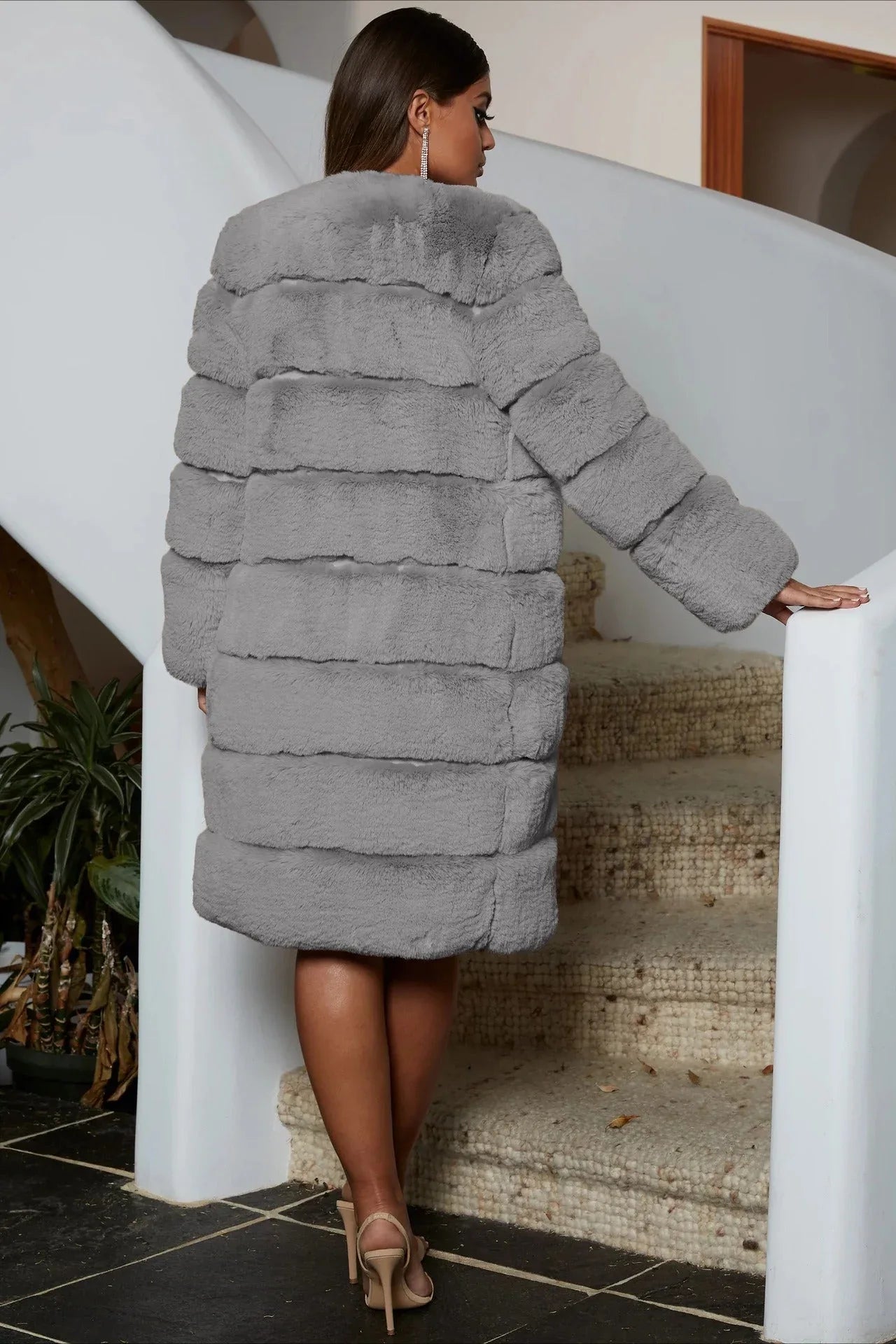 Rear view of a woman wearing a gray faux fur coat and heels on a staircase.
