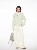 Woman wearing a light green hooded cardigan with white pants and a silver bag, full body front view