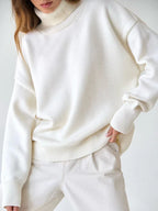 Close-up of a woman wearing a white oversized turtleneck sweater and beige pants, with her hand in her pocket.