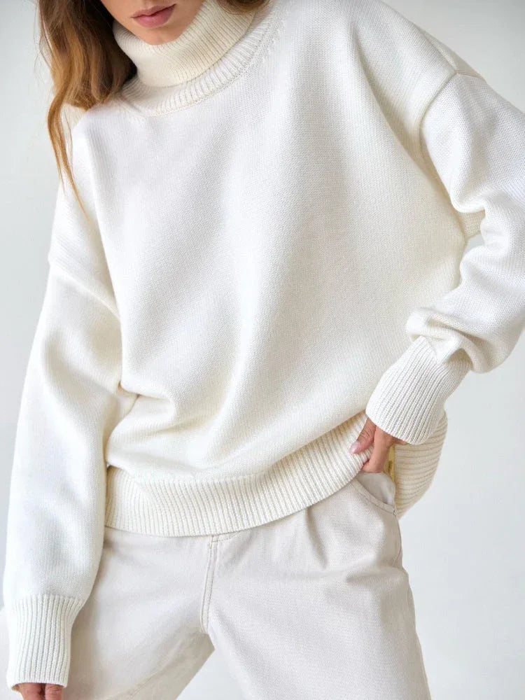 Close-up of a woman wearing a white oversized turtleneck sweater and beige pants, with her hand in her pocket.