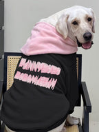 Side view of a Labrador retriever wearing a black hooded sweatshirt with pink text graphic and pink hood lining.