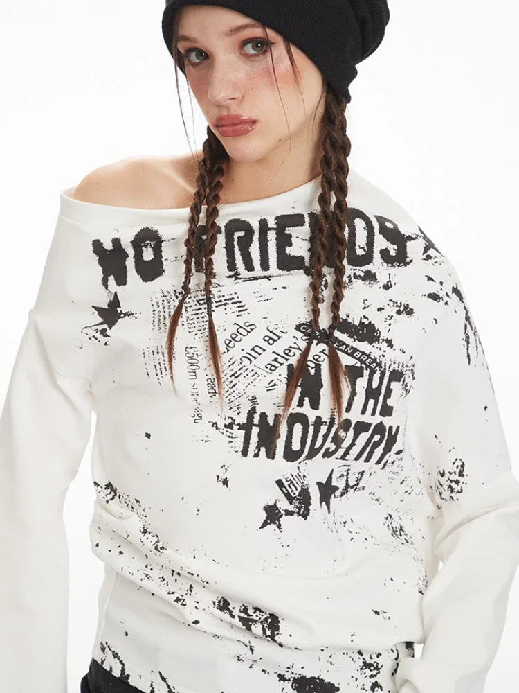 Extreme close-up of the graphic print on a white long-sleeved off-the-shoulder top.