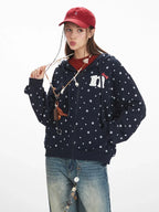 Front close-up of a woman wearing a navy blue hooded zip-up jacket with a white paw print pattern and a graphic detail on the chest, holding a necklace.