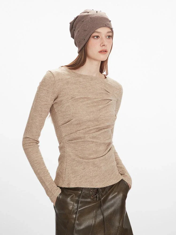 Close-up of a woman wearing a beige long-sleeve knit top with ruched detailing and a beige beanie adorned with studs.