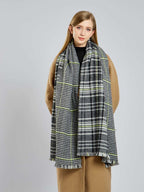 Woman wearing a tan coat and a large houndstooth and plaid scarf with fringed edges