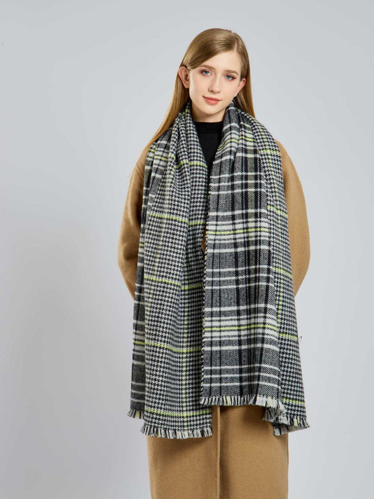Woman wearing a tan coat and a large houndstooth and plaid scarf with fringed edges