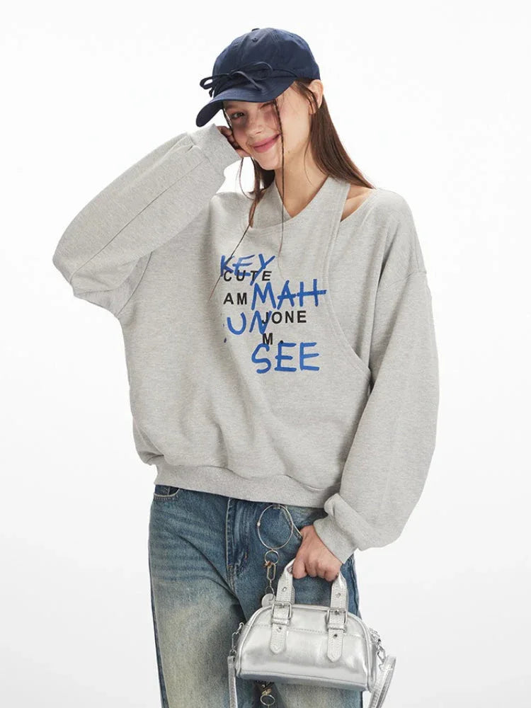 Close-up of model wearing a grey graphic print sweatshirt, smiling and touching her hat