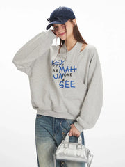 Close-up of model wearing a grey graphic print sweatshirt, smiling and touching her hat
