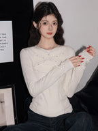 Woman wearing a white long-sleeved top with ruffled trim and beaded embellishments, paired with dark wash jeans.