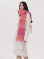 Woman wearing a white sweater and a long pink and orange gradient scarf with fringe.