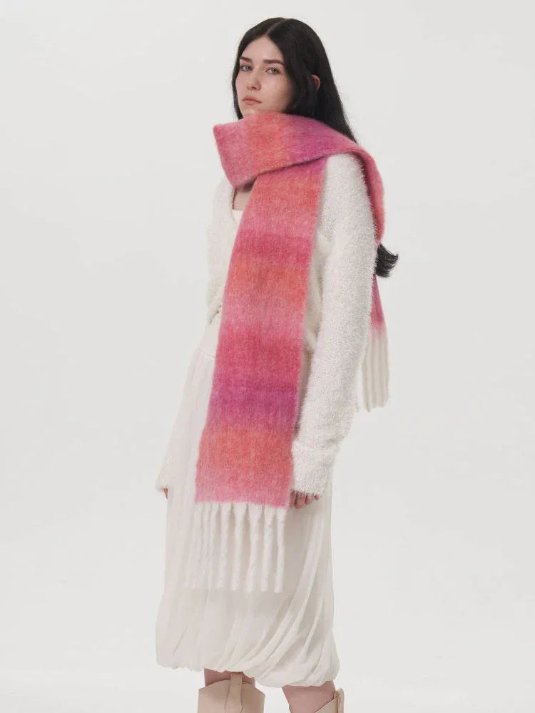 Woman wearing a white sweater and a long pink and orange gradient scarf with fringe.