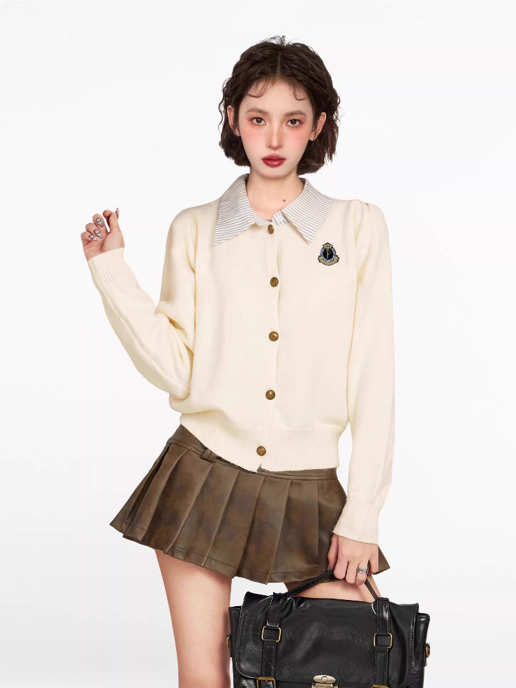 Woman wearing a cream-colored knit cardigan over a striped collared shirt, paired with a brown pleated skirt and a black handbag.