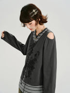 Side view of a model wearing a grey long-sleeve top with cold shoulder cutouts and a graphic print, layered over a striped t-shirt.