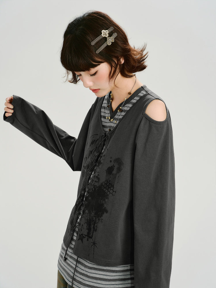 Side view of a model wearing a grey long-sleeve top with cold shoulder cutouts and a graphic print, layered over a striped t-shirt.