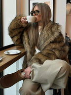 Woman drinking coffee while wearing a brown faux fur jacket and beige pants.