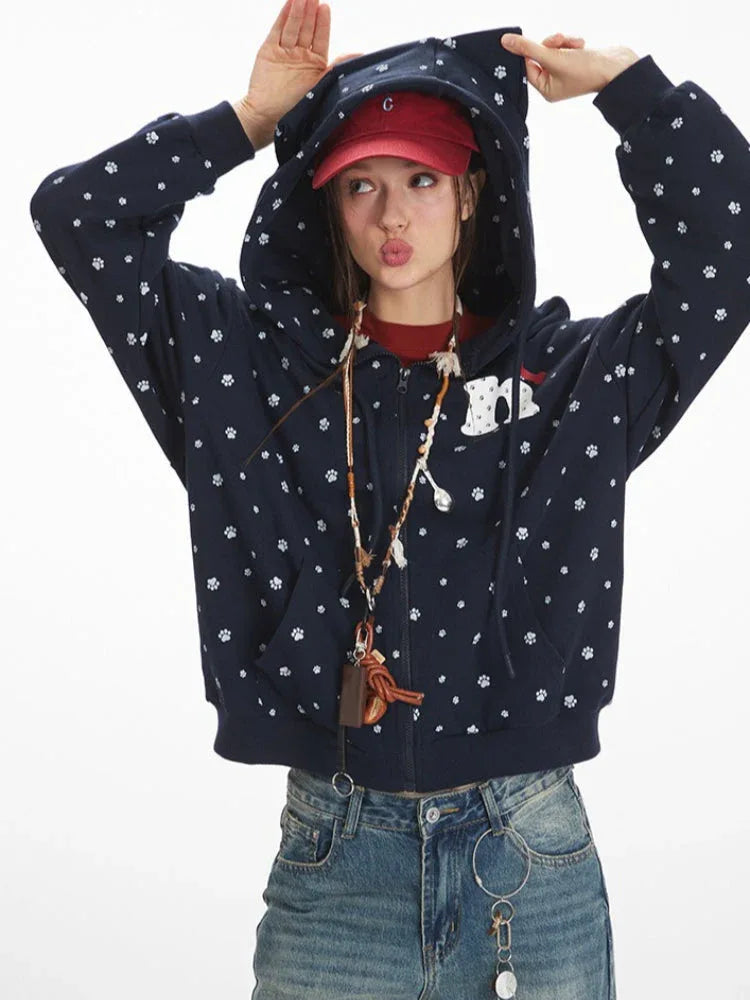 Woman wearing a navy blue hooded zip-up jacket with a white paw print pattern, pulling up the hood.
