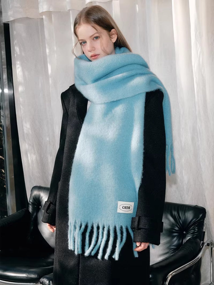 Woman wearing a light blue fluffy knit scarf with fringe detail and a black coat.