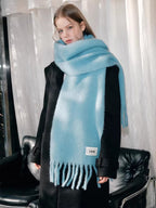 Woman wearing a light blue fluffy knit scarf with fringe detail and a black coat.