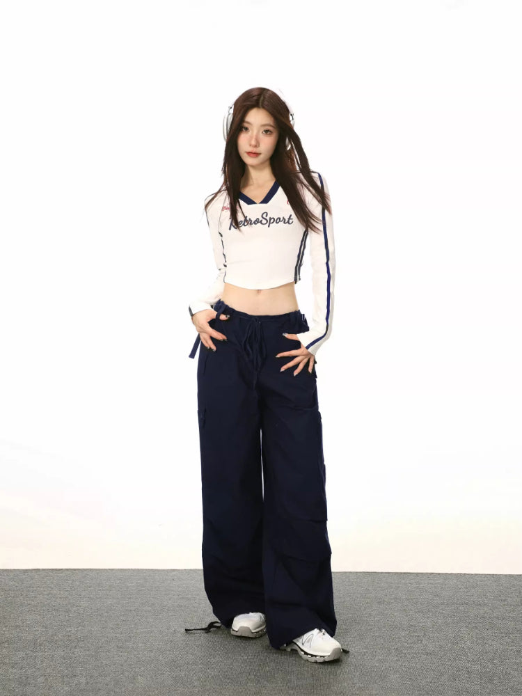 Full body shot of a woman in a white cropped long-sleeve shirt and navy cargo pants, styled with headphones.