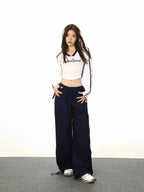 Full body shot of a woman in a white cropped long-sleeve shirt and navy cargo pants, styled with headphones.