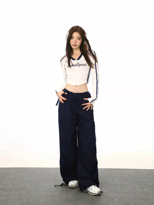 Full body shot of a woman in a white cropped long-sleeve shirt and navy cargo pants, styled with headphones.