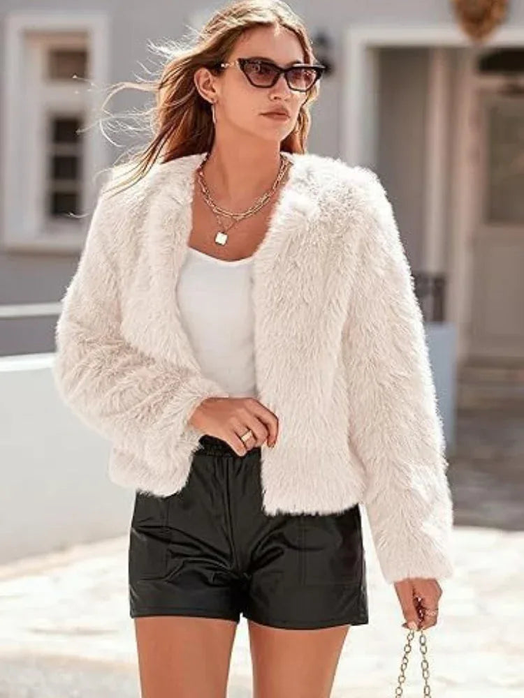 Woman wearing a white faux fur cropped jacket over a white top and black shorts, accessorized with sunglasses and a necklace. Main image