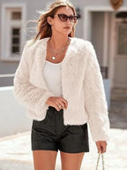 Woman wearing a white faux fur cropped jacket over a white top and black shorts, accessorized with sunglasses and a necklace.