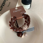 A single set of Henju hair ties with a heart charm and decorative beads, placed on a white dish.