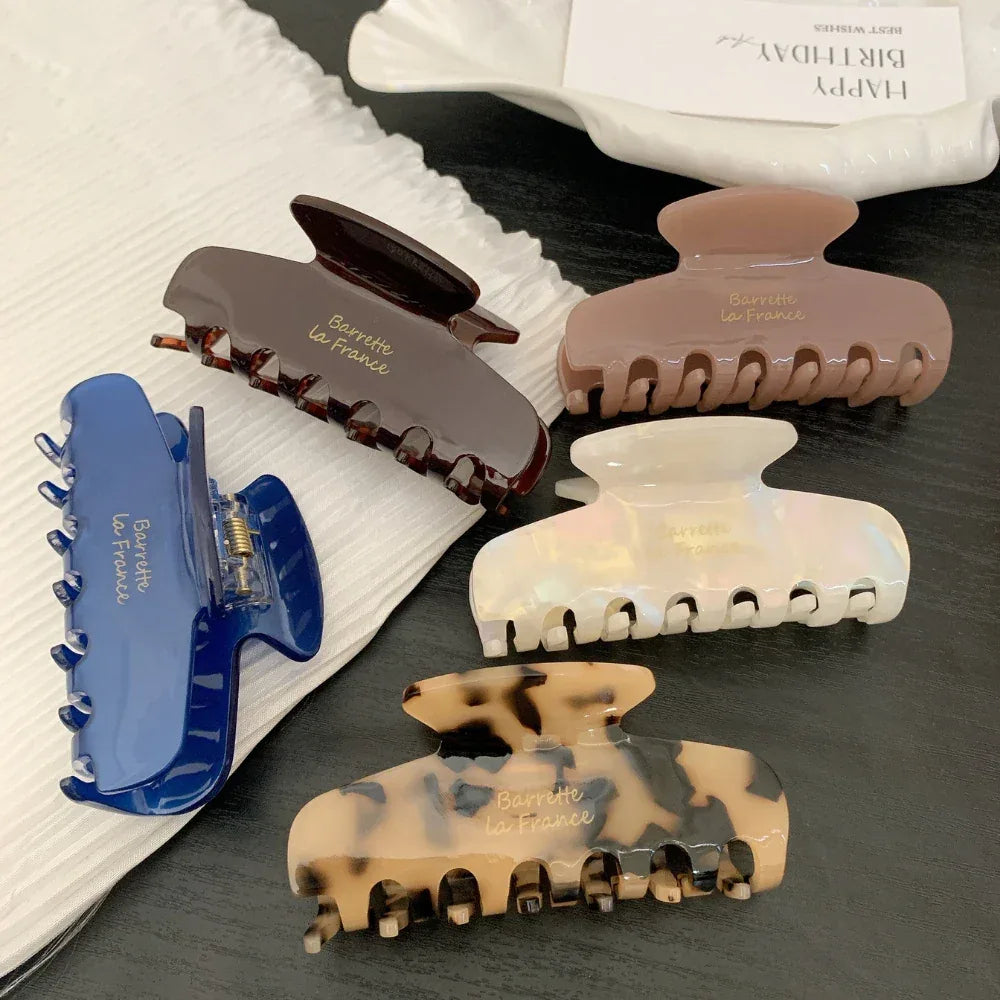 Several hair claw clips in different colors and finishes are laid out on a white cloth and a dark surface.