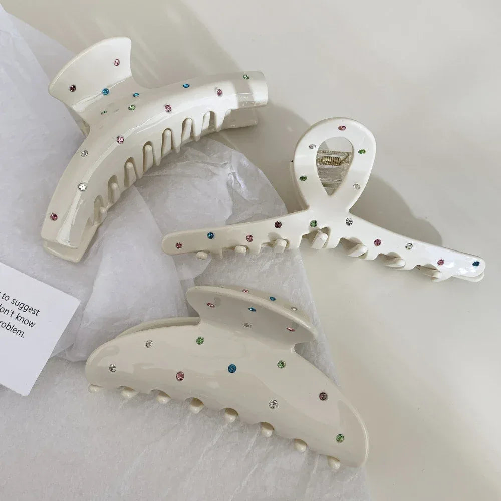 Three cream-colored claw clips with colorful gemstones on white tissue paper