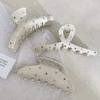 Three cream-colored claw clips with colorful gemstones on white tissue paper