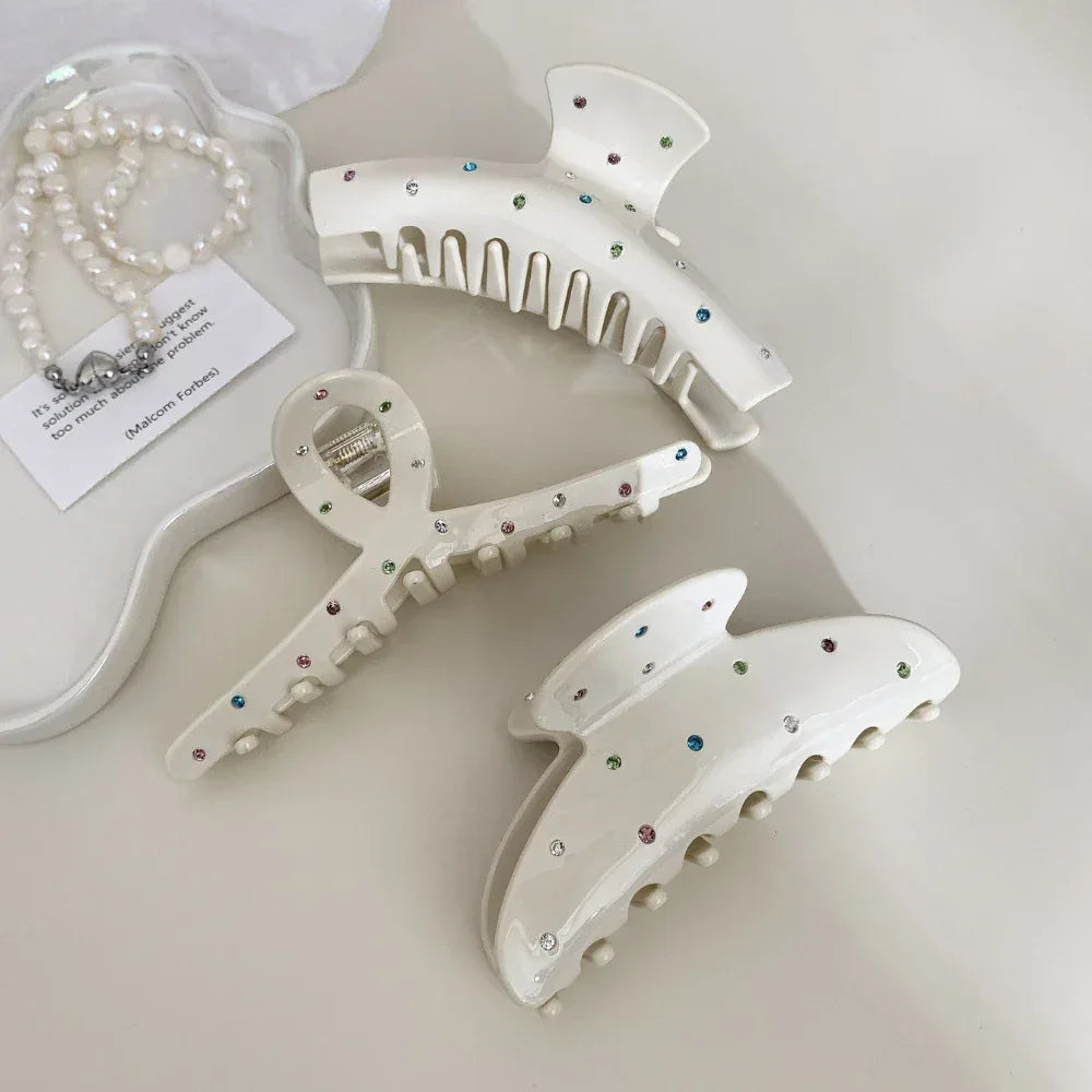 Three cream-colored claw clips with colorful gemstones and a pearl necklace