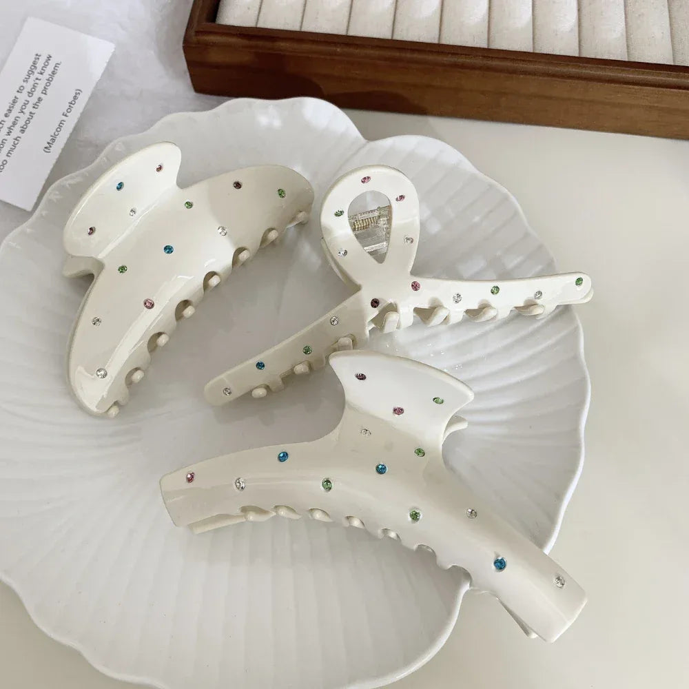 Three cream-colored claw clips with colorful gemstones arranged on a plate