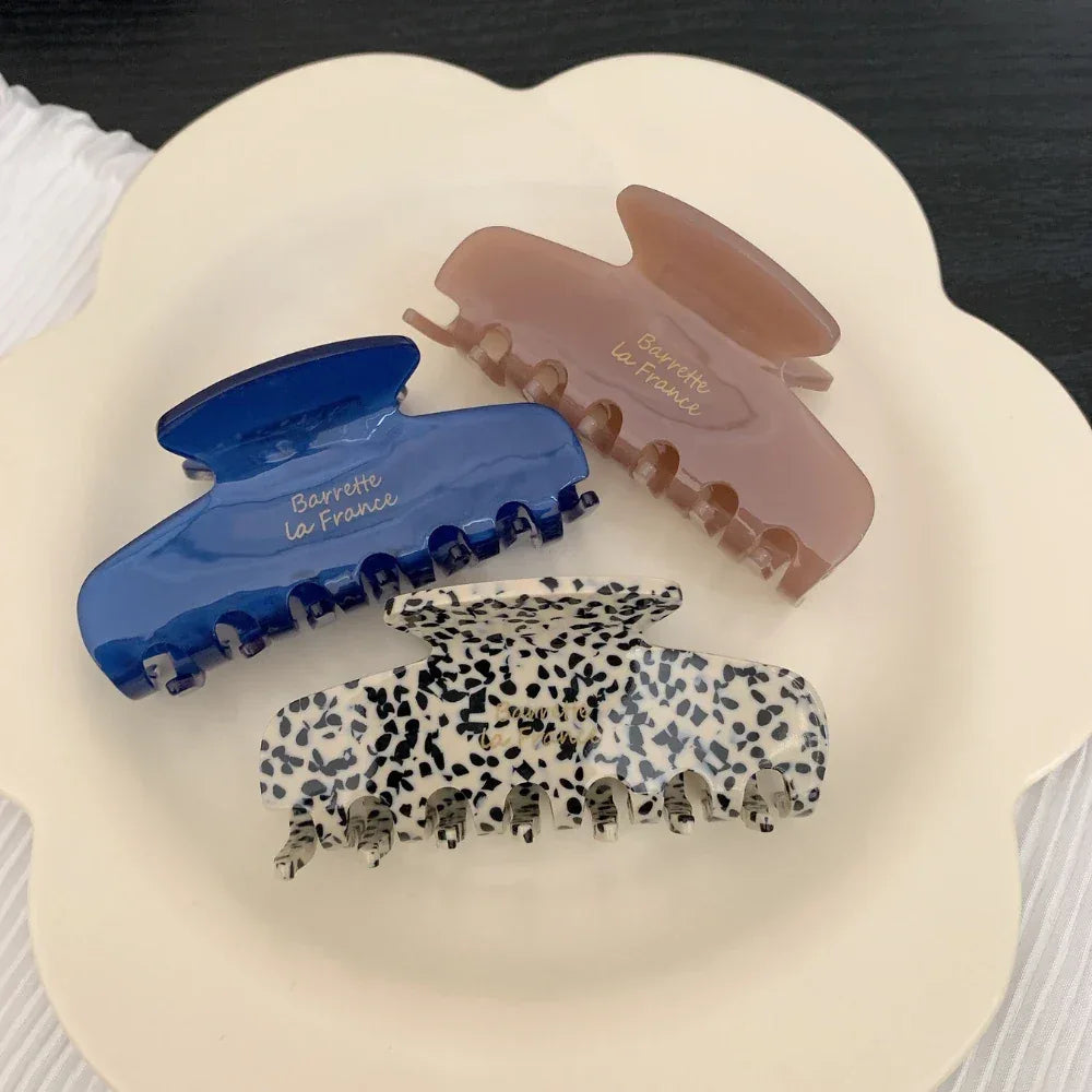 Three hair claw clips in blue, leopard print, and pinkish-brown, arranged on a white scalloped plate.