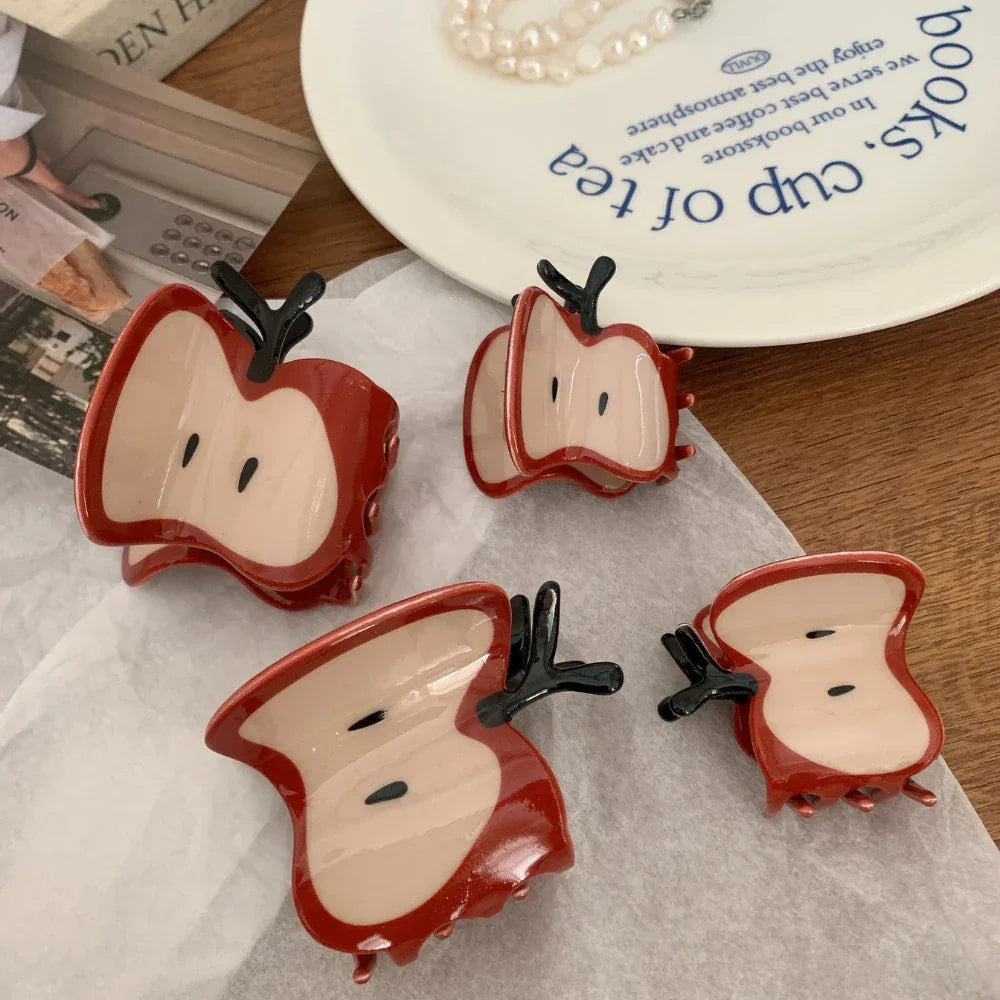An overhead view of four apple slice hair claw clips on a wooden surface, showcasing their design and size variations.