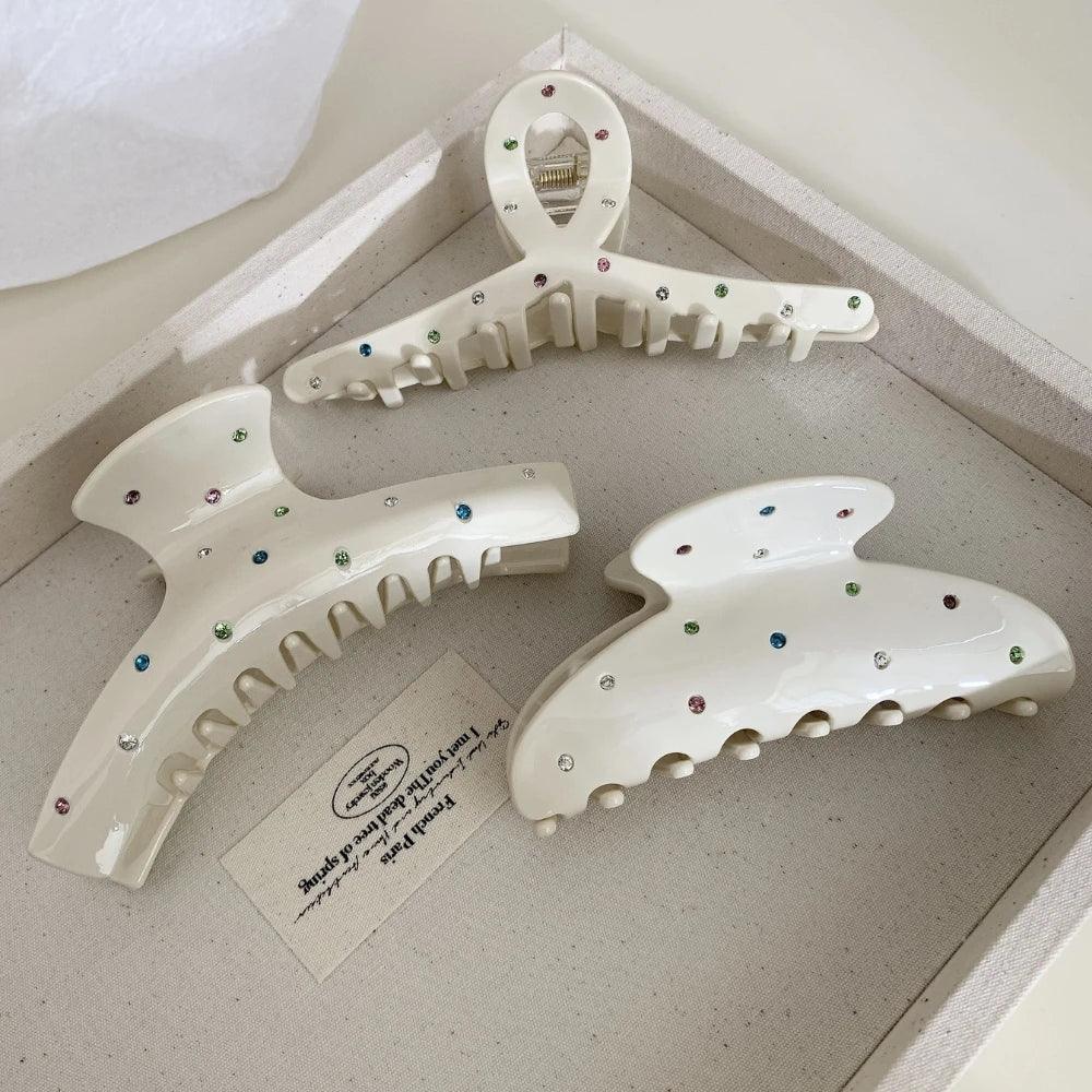 Three cream-colored claw clips with colorful gemstones on a tray