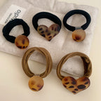 A collection of hair ties on a fabric cloth. Some have round charms, others have heart-shaped charms, and they are in black and brown colors.