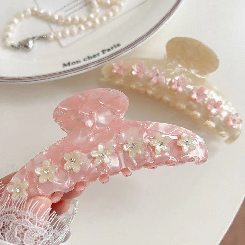 A hand holding a pink marbled claw clip decorated with white flowers and gemstones.