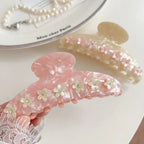 A hand holding a pink marbled claw clip decorated with white flowers and gemstones.