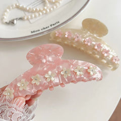A hand holding a pink marbled claw clip decorated with white flowers and gemstones.