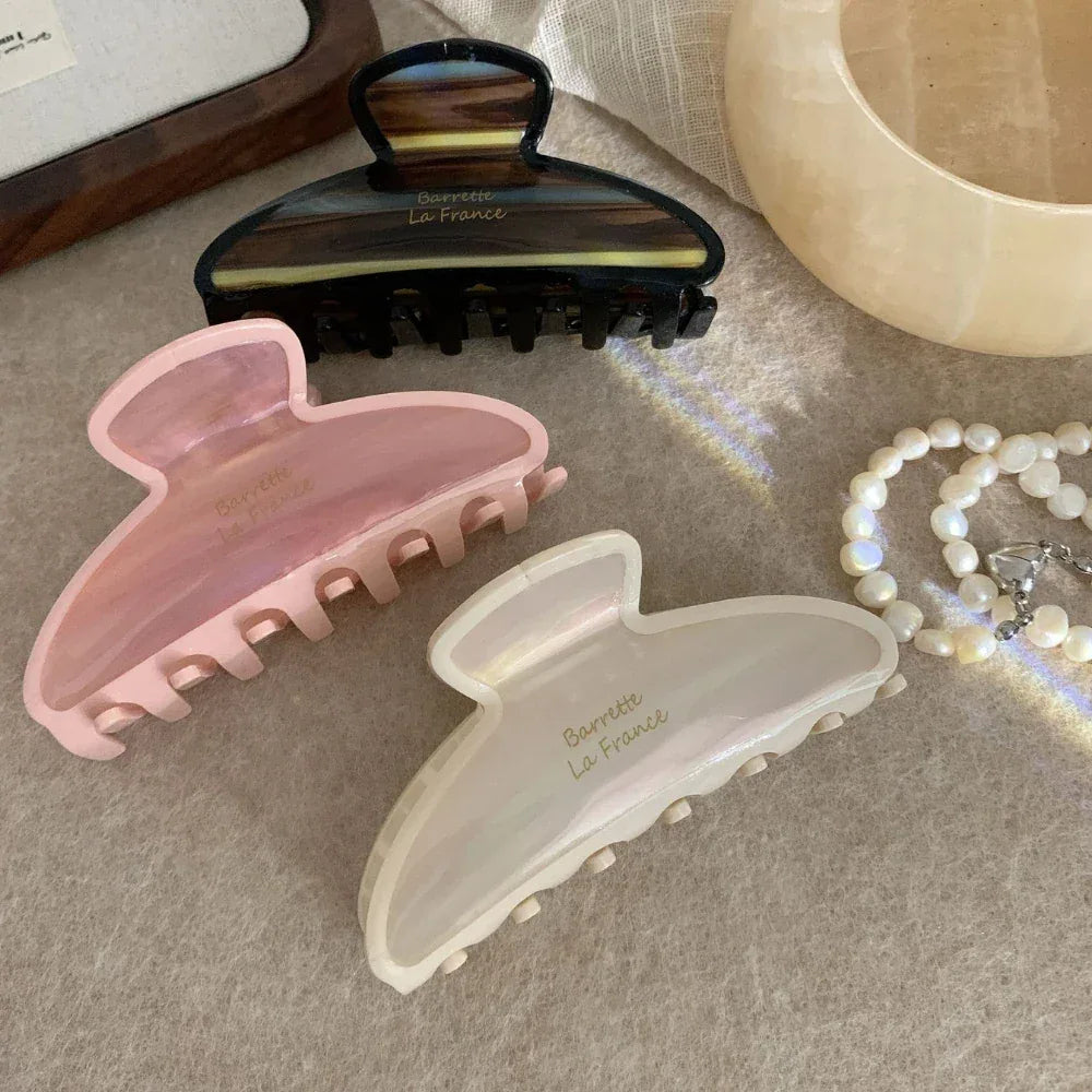 Three claw clips in pink, cream, and brown tortoiseshell patterns arranged on a textured surface.