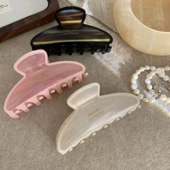 Three claw clips in pink, cream, and brown tortoiseshell patterns arranged on a textured surface.