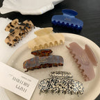 A variety of hair claw clips displayed on a white tray and a dark surface, featuring different patterns and colors.