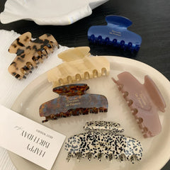 A variety of hair claw clips displayed on a white tray and a dark surface, featuring different patterns and colors.