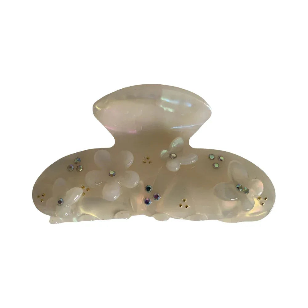 Opaque white claw clip with iridescent sheen, adorned with white floral appliques, small rhinestones, and gold beads. Main image