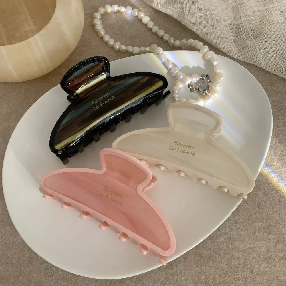 Three claw clips in pink, cream, and brown tortoiseshell patterns arranged on a white plate with a pearl necklace.