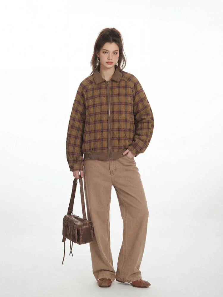 Woman wearing a plaid bomber jacket and tan pants, holding a brown bag.