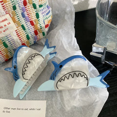Two blue and white shark hair clips next to a woven bag