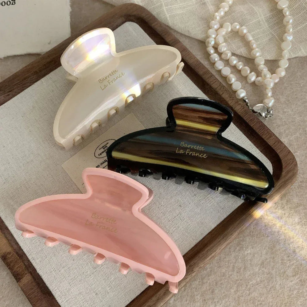 Three claw clips in pink, cream, and brown tortoiseshell patterns arranged on a wooden tray.