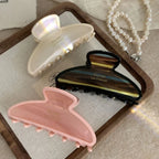 Three claw clips in pink, cream, and brown tortoiseshell patterns arranged on a wooden tray.